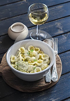 Orecchiette pasta with broccoli and pine nuts pesto and a glass of white wine on dark wooden background.