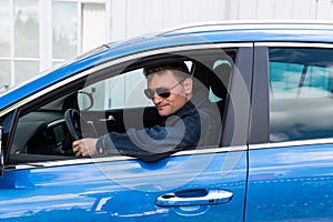 Oregrund, Uppland - Sweden -Fourty year old fashionable man with sunglasses posing in his blue Kia Sportage car