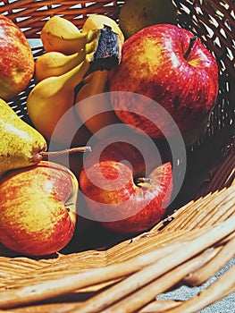 Organic apples, pears and bananas on rustic in a wicker basket