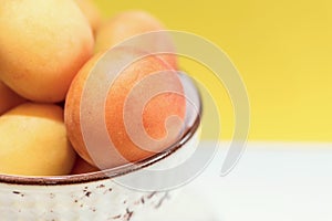 Organic apricots in a ceramic bowl on a white table in front of the yellow background, close up