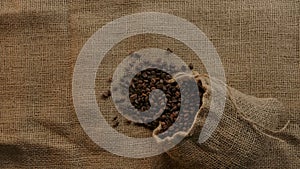 Organic authentic jute bag with roasted coffee beans falling in slow motion on burlap background.