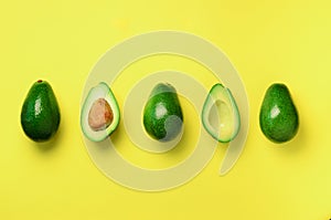 Organic avocado with seed, avocado halves and whole fruits on yellow background. Top view. Pop art design, creative