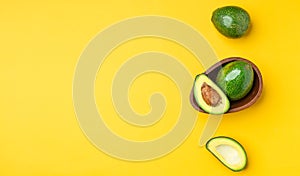 Organic avocados half cut with seed and whole fruit in wood bowl on yellow table background.Healthy super foods for diet.Fresh