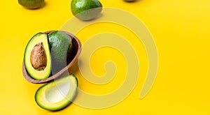 Organic avocados half cut with seed and whole fruit in wood bowl on yellow table background.Healthy super foods for diet.Fresh