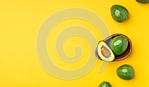 Organic avocados half cut with seed and whole fruit in wood bowl on yellow table background.Healthy super foods for diet.Fresh