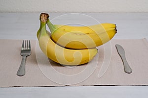 Organic banana fruits on beige linen fabric on the table with eating utensils