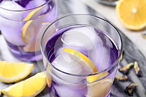 Organic blue Anchan with lemon and ice cubes on table, closeup. Herbal tea