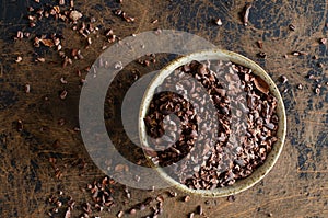 Organic cacao nibs from Peru in clay bowl on abstract wooden background