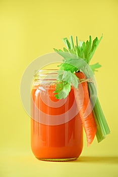 Organic carrot juice with carrots, celery on yellow background. Vegetable smothie in glass jar. Copy space. Summer food