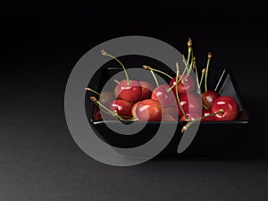 Organic cherries in a black bowl. Ripe berries on a black background.