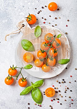 Organic Cherry Orange Rapture Tomatoes on the Vine with basil and pepper on chopping board on stone kitchen background.