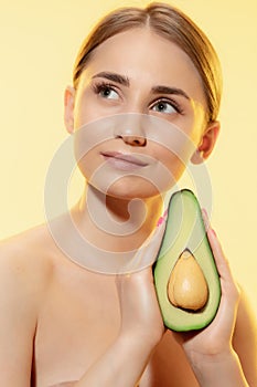 Organic. Close up of beautiful female face with half avocado over yellow background. Cosmetics and makeup, natural and