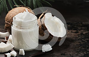 Organic coconut oil and coconuts, close-up on a metal background. Selective focus on oil in a jar. Skin and body care
