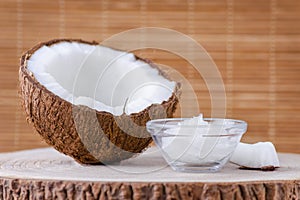 Organic coconut oil in a glass bowl and coconut on natural brown background