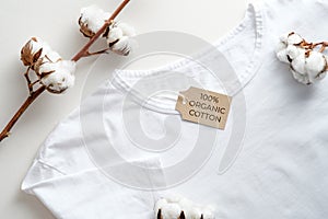 Organic cotton white t-shirt and cotton flowers on table top view. Eco clothing, sustainable lifestyle concept