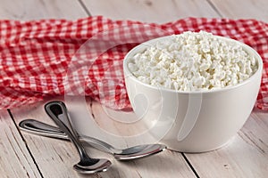 Organic curd cottage cheese in a white ceramic bowl and red napkin on a wooden table