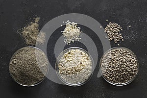 Organic dried hemp seeds , flour, kernels in black bowls on dark background. View from above