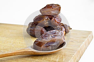 Organic dried hurma dates medjool grains, in wooden spoon on cutting board