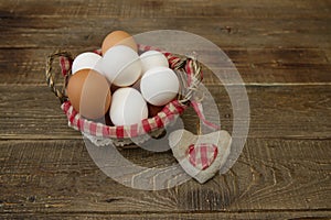 Organic eggs in a basket with a decorated checkered napkin and a heart made of linen fabric on a wooden rustic background