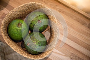 Organic farm avocado in straw basket on wooden table closeup. Fresh ripe green exotic fruits