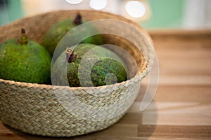 Organic farm avocado in straw basket on wooden table closeup. Fresh ripe green exotic fruits