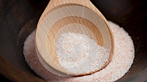 Organic fine grain pink Himalayan salt crystals falling onto a wooden spoon in a rustic bowl in slow motion close up