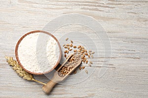 Organic flour in bowl, scoop with grains of wheat and spikelet on wooden table, flat lay. Space for text