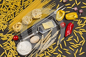 Organic food  on black background. Variety of types and shapes of dry Italian pasta with vegetables tomatoes, yellow and red
