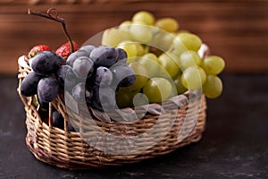 Organic fresh berries of green grapes, strawberries, raspberries, blue blueberries in a basket on a dark concrete background.