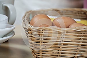 Organic fresh eggs in woven basket, white cups on a wooden table