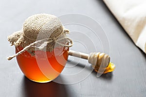 Organic fresh liquid honey in glass jar with dipper on rustic background