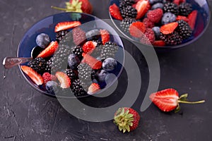 Organic fresh ripe blackberries, strawberries, raspberries, blueberries in blue saucers on a dark concrete background.