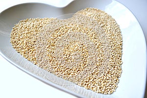 Organic gluten free quinoa grain in a heart shaped bowl on white with copy space