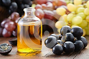 Organic grape seeds essential oil bottle. Black, green and purple grapes on table