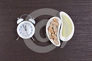 Organic herbal pills and dried leaf plant powder with alarm on wooden background.