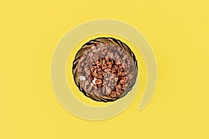 Organic homemade roasted granola cereal with oats, flax, almonds, chocolate in round glass bowl on yellow background. Top view