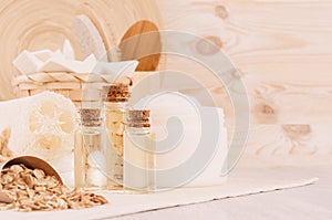 Organic homemade white cosmetics, bottles with oil and raw oatmeal flakes, bath accessories on light beige wooden background.