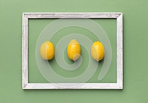 Organic lemons inside wooden frame on light green