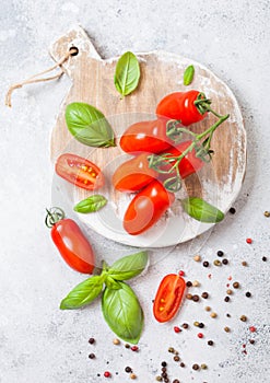 Organic Mini San Marzano Tomatoes on the Vine with basil and pepper on chopping board on white kitchen background