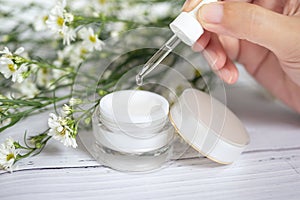 Organic natural skincare concept. open blank cosmetic cream jar with white cream texture inside and women hand holding dropper photo