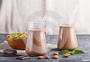 Organic non dairy almond chocolate milk in glass and wooden plate with almond nuts on a black concrete background