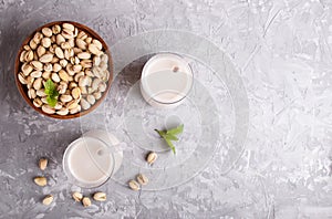 Organic non dairy pistachio milk in glass and wooden plate with pistachionuts on a gray concrete background photo