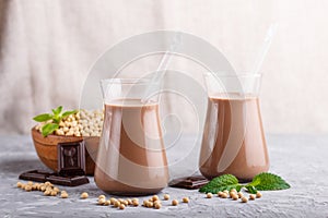 Organic non dairy soy chocolate milk in glass and wooden plate with soybeans on a gray concrete background