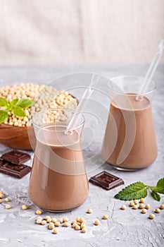 Organic non dairy soy chocolate milk in glass and wooden plate with soybeans on a gray concrete background