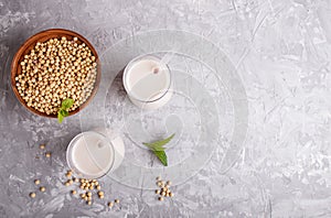 Organic non dairy soy milk in glass and wooden plate with soybeans on a gray concrete background