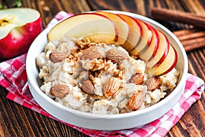 Organic oatmeal porridge in white ceramic bowl with apple, almond, honey and cinnamon. Healthy breakfast