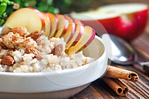 Organic oatmeal porridge in white ceramic bowl with apple, almond, honey and cinnamon Healthy breakfast.