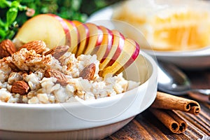 Organic oatmeal porridge in white ceramic bowl with apple, almond, honey and cinnamon. Healthy breakfast