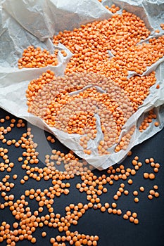 Organic orange lentils scattered on white paper and black background