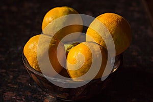 Organic oranges freshly plucked from farm is arranged on a wooden bowl isolated on a black background.